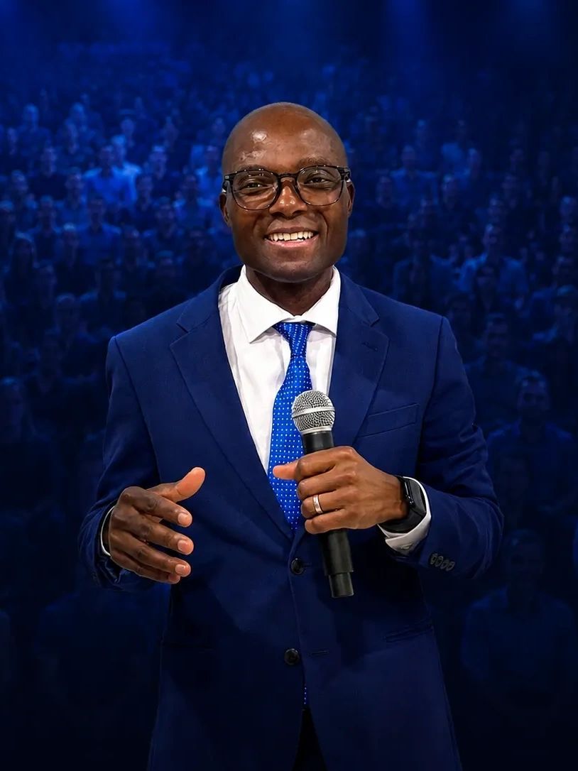 Man in blue suit speaking with a microphone on stage.