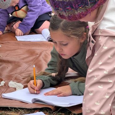 Children outdoors focused on writing and drawing in notebooks.