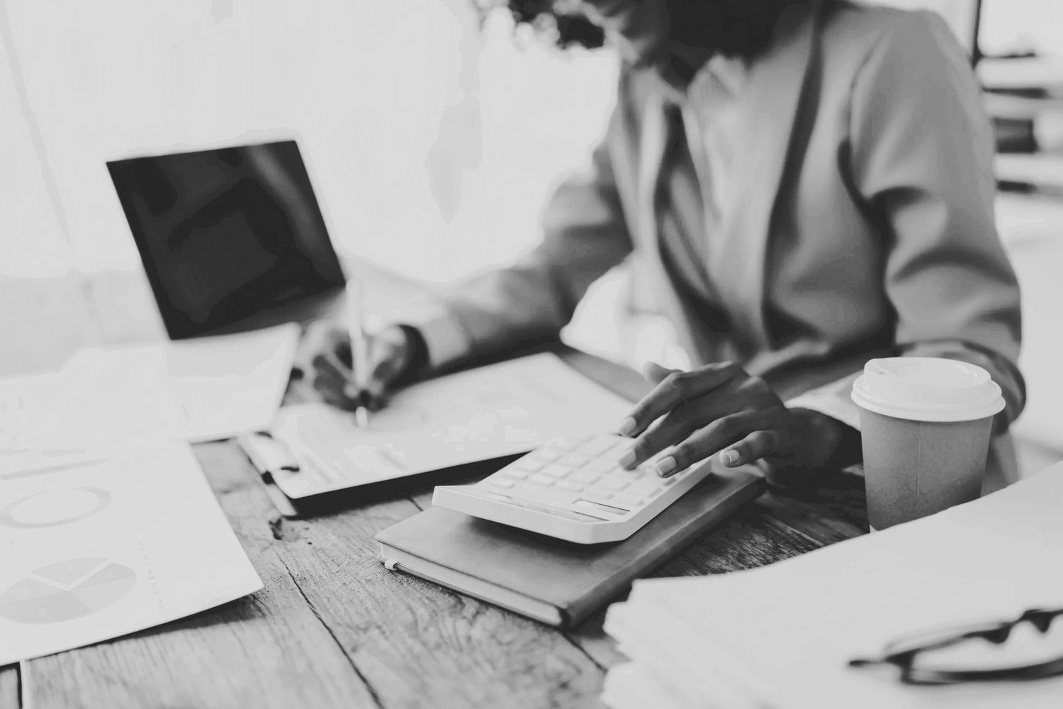 Person working with calculator and paperwork at a desk with coffee.
