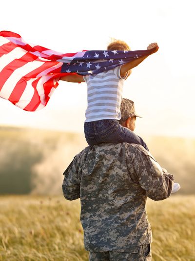 I U.S. Army Soldier in Army Combat Uniform, with child on his shoulders and a U.S. Flag waiving. 