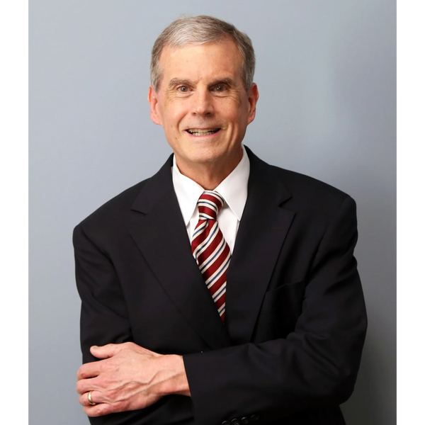 Smiling mature man in a suit with a striped tie against a gray background.