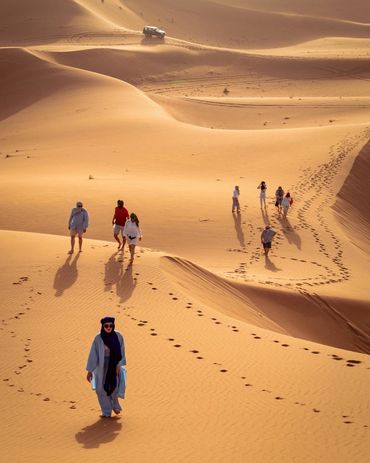 People trekking across vast desert sand dunes under the sun.