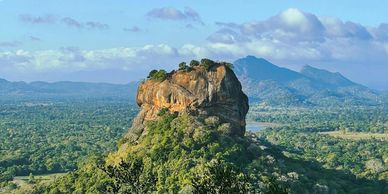 A large rock formation in a green valley under a cloudy sky.
