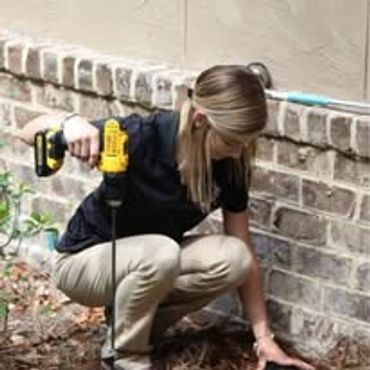 Woman using a drill near a brick wall outdoors.