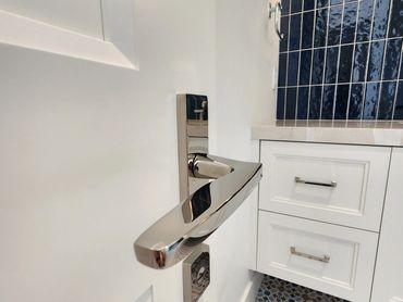 Close-up of a modern chrome door handle in a white bathroom with patterned blue and white floor tiles.