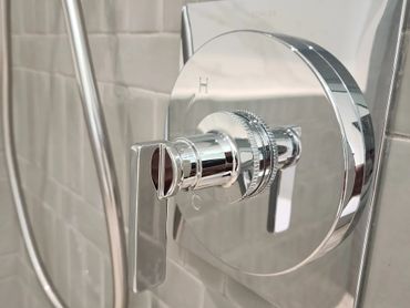 Close-up of a shiny chrome shower control handle on a tiled wall.