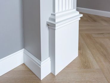 Close-up of white decorative baseboard and molding on light wood floor.