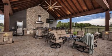 Spacious outdoor patio with seating, kitchen, and fireplace under a wooden roof.