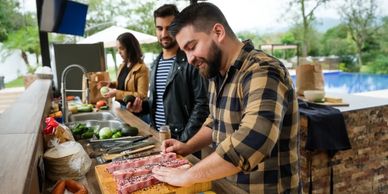 Three people preparing food outdoors by a poolside kitchen.