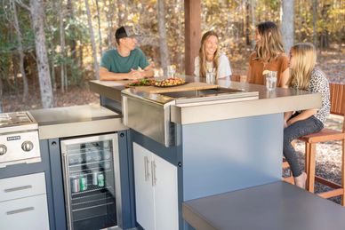 Family enjoying a meal at an outdoor kitchen in a wooded backyard.