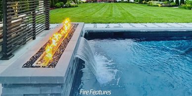 Modern pool with fire feature and waterfall edge in a landscaped backyard.