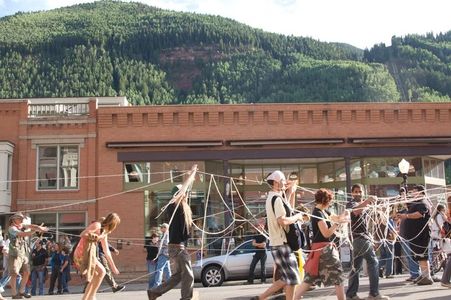 A group of people walk through a street tangled in strings or yarn.