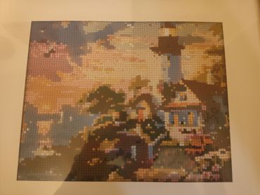Pixelated artwork of a lighthouse and houses at sunset.