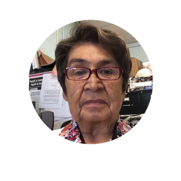 Elderly woman wearing glasses, sitting indoors with a serious expression.