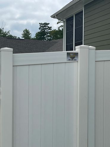 White vinyl privacy fence with a security sign and house in background.