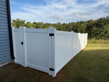 White vinyl privacy fence enclosing a backyard area beside a house.