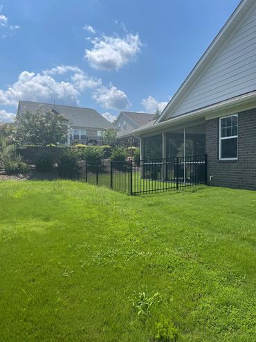 Sunny backyard with green grass and a fenced patio attached to a house.