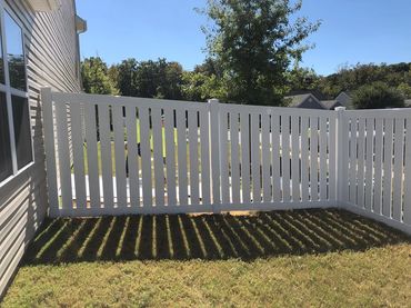 White fence casting striped shadows on grass under clear sky.