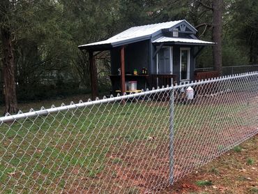 Small gray shed behind a chain-link fence in a grassy yard.