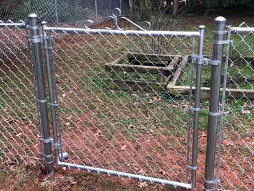 A metal chain-link fence with a gate and garden beds behind it.