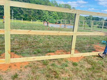 Newly constructed wooden and wire fence in a grassy field with a person walking nearby.