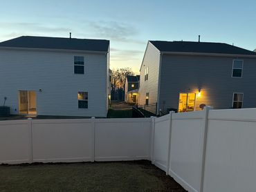 White fenced backyard with houses at dusk.