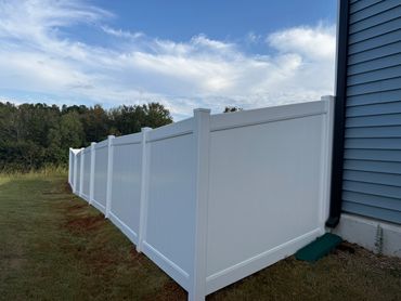Long white vinyl privacy fence alongside a blue house under a partly cloudy sky.