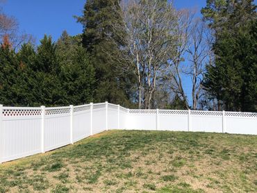 White vinyl fence enclosing a grassy yard with trees in the background.