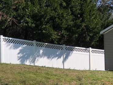 White vinyl fence with lattice top panels beside a beige shed and grassy hill.