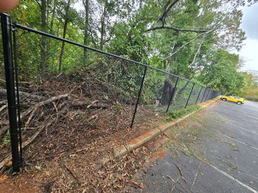 A damaged black chain-link fence next to a parking lot with a yellow car.