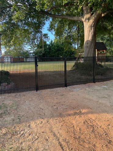 Black metal fence with a large tree and playground in the background.