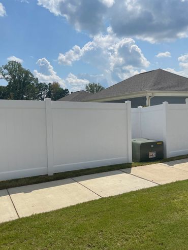 White vinyl fence along a sidewalk with houses and blue sky.