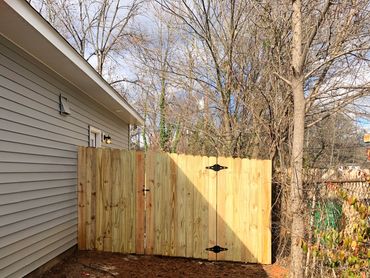 Newly installed wooden gate attached to a house with a dirt yard.
