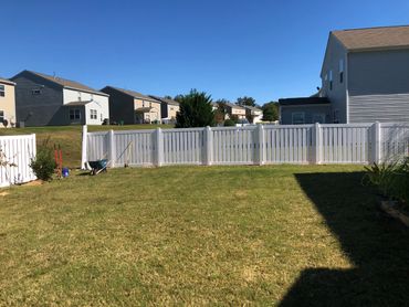 A sunny backyard with a white fence and gardening tools.