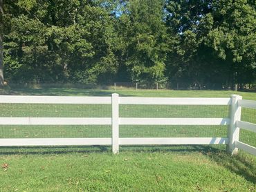 White wooden fence enclosing a green grassy area with trees in the background.