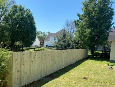 New wooden privacy fence in a sunny backyard with green trees.