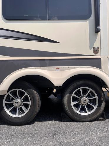 Close-up of dual wheels on a beige and gray RV with broken leaf springs. Axle repair