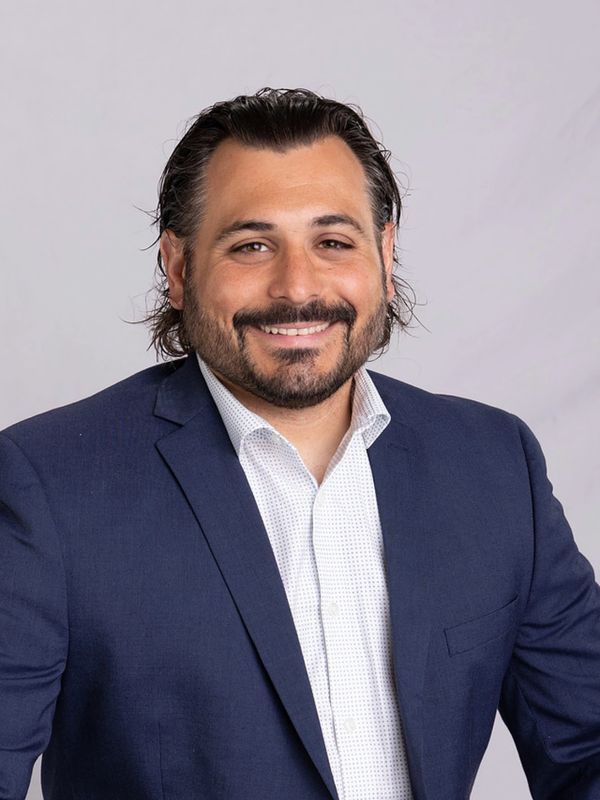 Man with beard and mustache smiling, wearing navy blazer and white shirt.