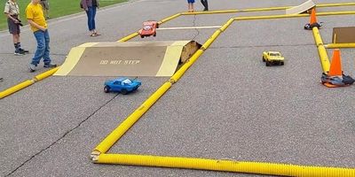 Kids watch remote-controlled cars on a makeshift race track outdoors.