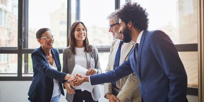 Female virtual COO smiles while shaking CEO's hand while 2 other people smile and observe