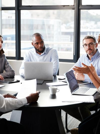 Male virtual COO leads meeting with operational team around conference table with laptops and papers