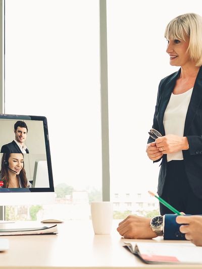 Female virtual CIO with CEO and staff at a conference table & people on PC attending virtually.