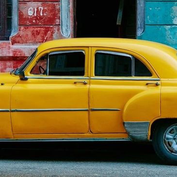 Bright yellow vintage car parked against colorful old buildings.