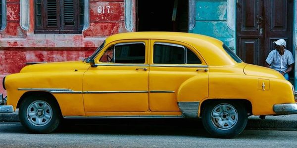 Bright yellow vintage car against colorful weathered walls.