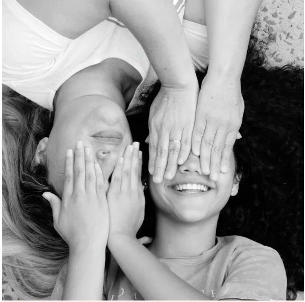 Two people lying down, covering their eyes playfully, smiling and relaxed.