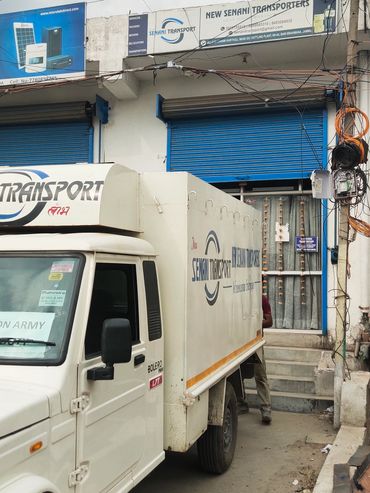 White transport truck parked near a building with blue shutters and signage.
