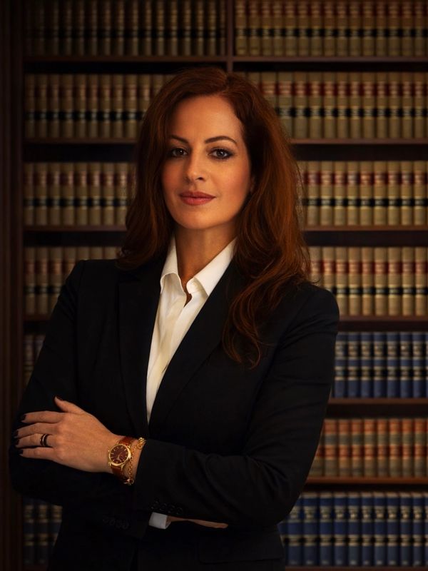 Confident woman in professional attire standing in front of legal bookshelves.