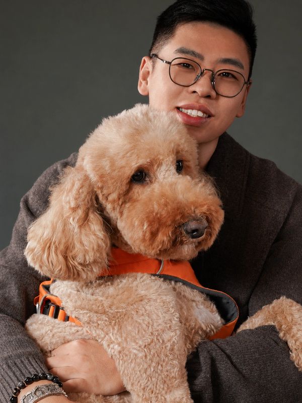 Man with glasses holding a fluffy dog in an orange vest.