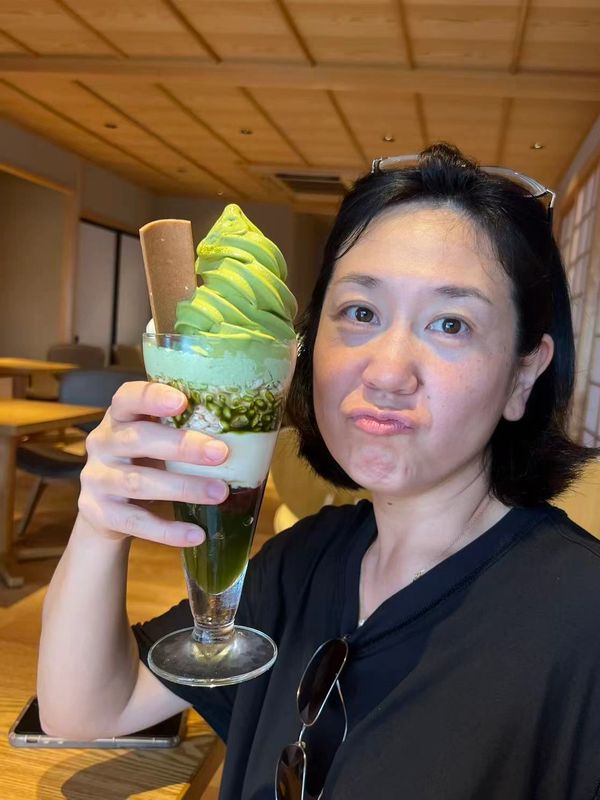 Woman holding a green tea dessert in a glass.