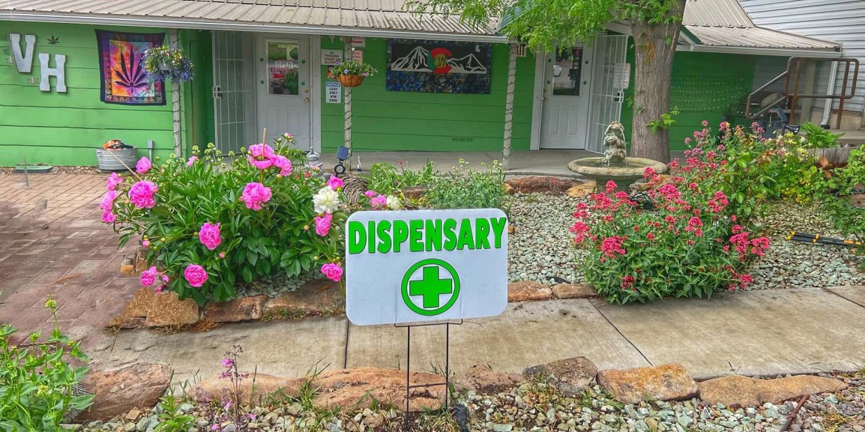 Dispensary sign with vibrant flowers in front of a green building.